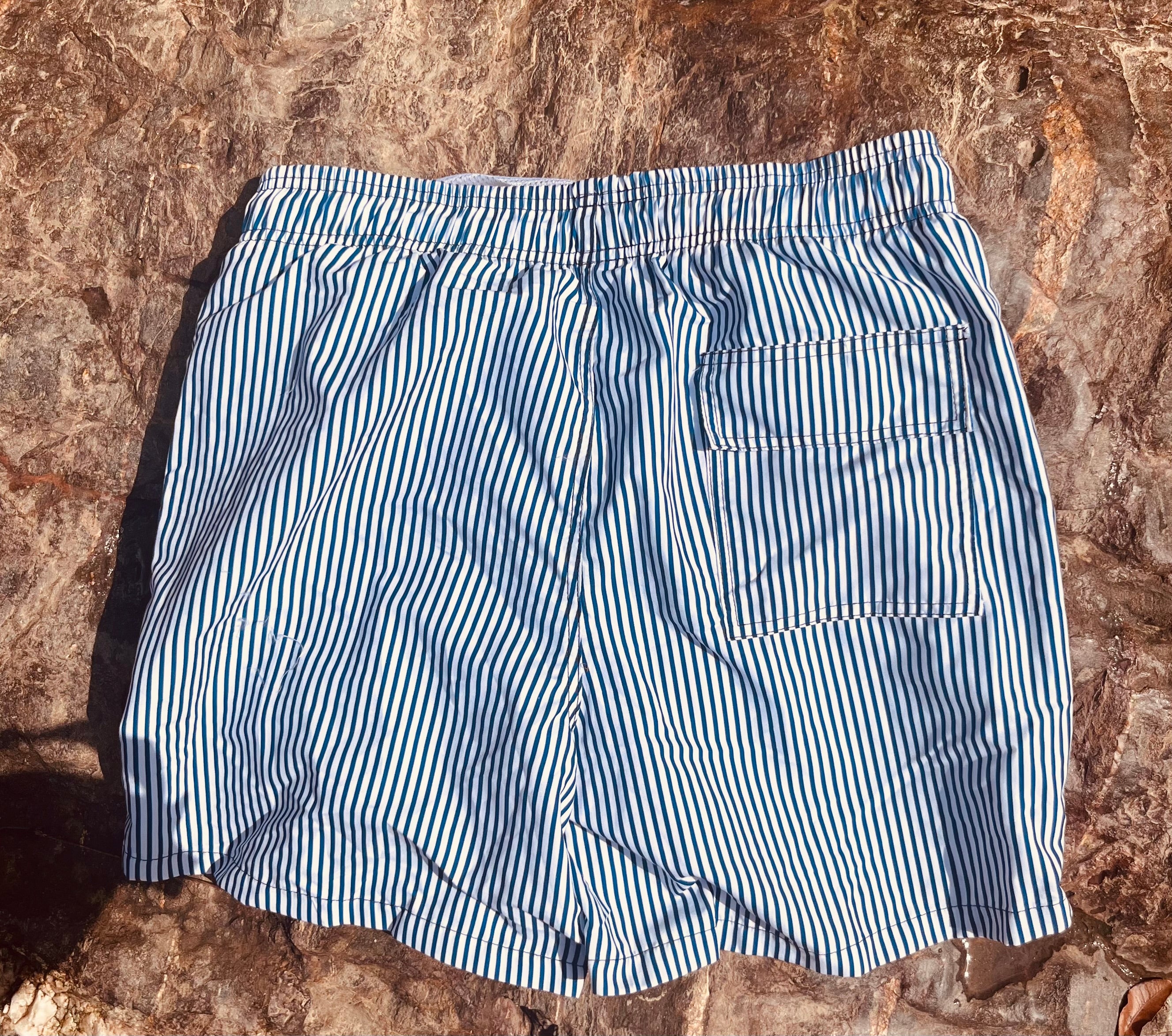 Backside of the Loa swimming shorts. White with blue stripes. Zipped pockets. 